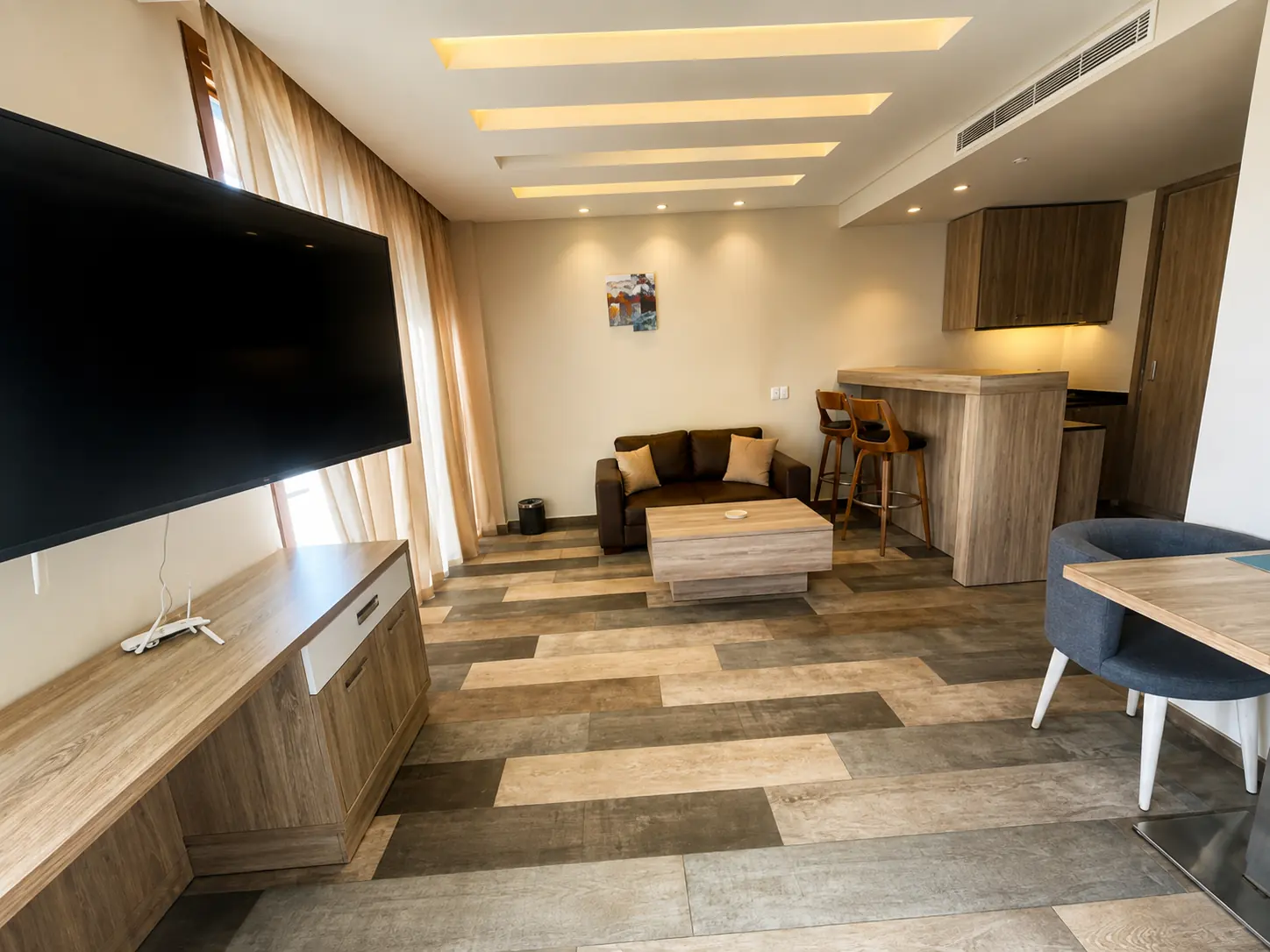 Modern hotel suite living area with kitchenette and TV